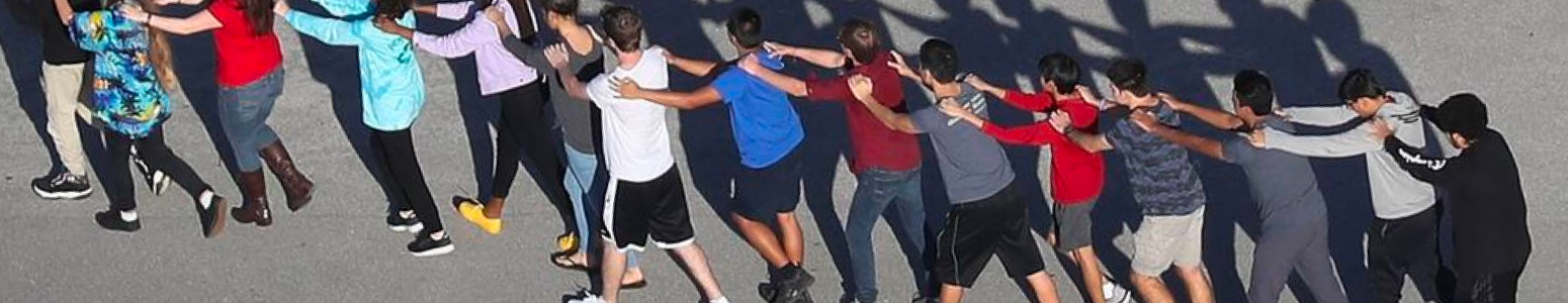 A line of students practice a drill by walking in a straight line, with hands on each others' shoulders