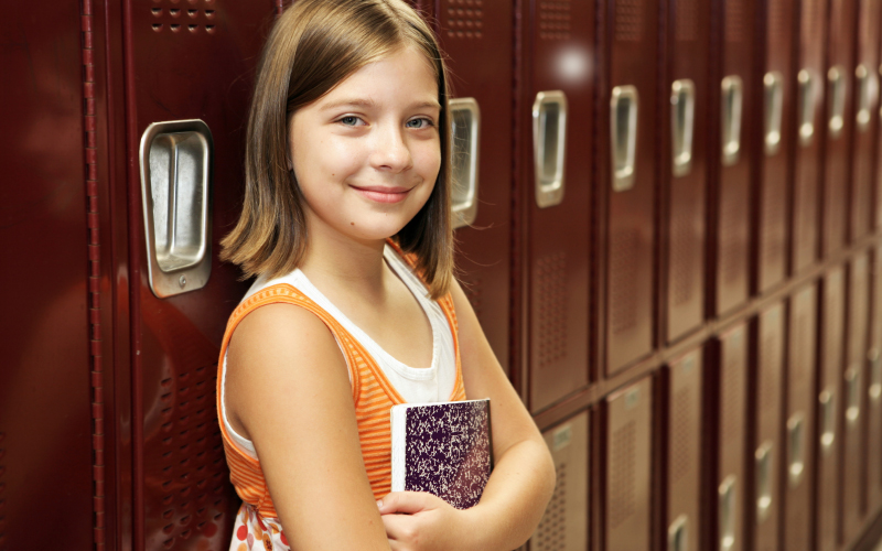 Elementary student smiling at the camera while standing in front of red lockers